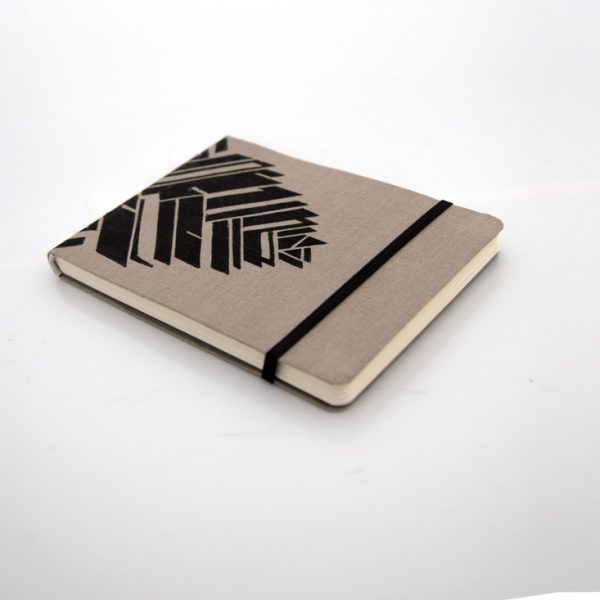 Libreta forrada en lino tono moca con estampado negro, elástico de cierre negro, cosida y encuadernada a mano sobre fonde grisáceo de la marca Leaftones creada por Diana Herrera Design