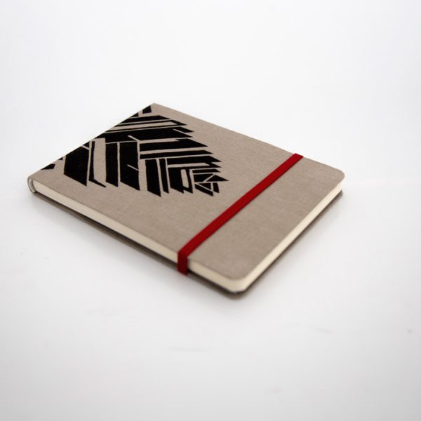 Libreta forrada en lino tono moca con estampado negro, elástico de cierre rojo, cosida y encuadernada a mano sobre fonde grisáceo de la marca Leaftones creada por Diana Herrera Design